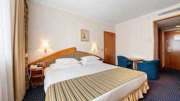 Habitación de hotel con una cama grande, lámparas de noche, una mesita, una silla y una puerta.