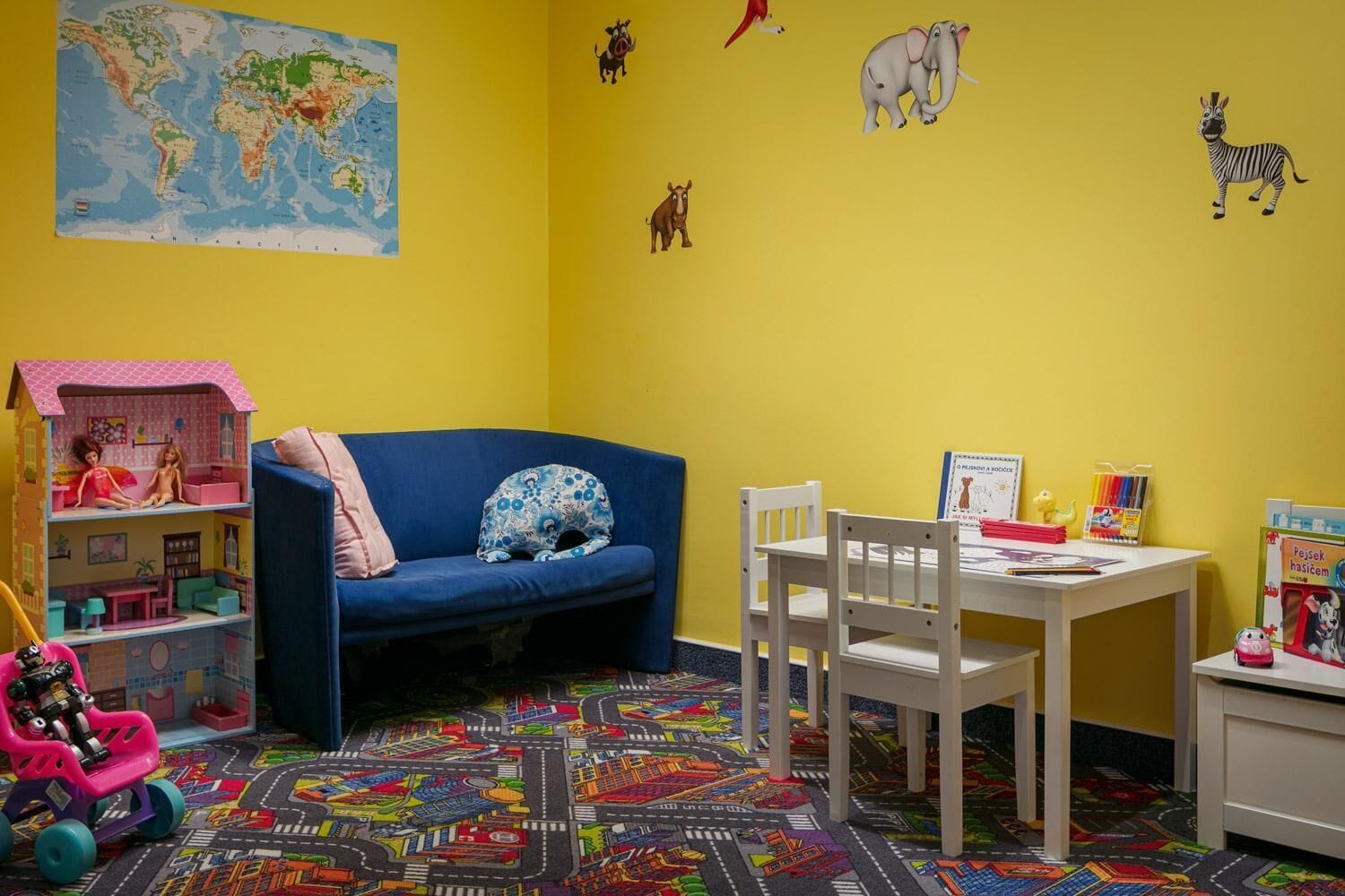 Un cuarto de juegos infantil con un mapa mundial, peluches, una casa de muñecas y un tapete de juegos colorido.