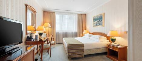 Una habitación de hotel con cama, mesita de noche, lámpara, televisor y escritorio con silla.