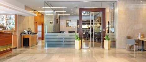 A hotel lobby with a reception desk, a seating area, and a glass partition.
