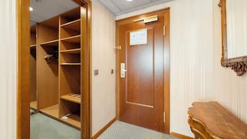 A hotel room with a wooden wardrobe, a small wooden table, and a door with a sign.