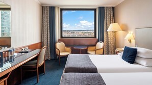 A hotel room with a bed, a desk, two chairs, a small table, and a view of the city. - Panorama by Verdi Hotels (Prague)
