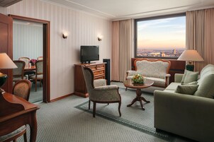 Een hotelkamer met een zithoek, televisie, bank en stadszicht.