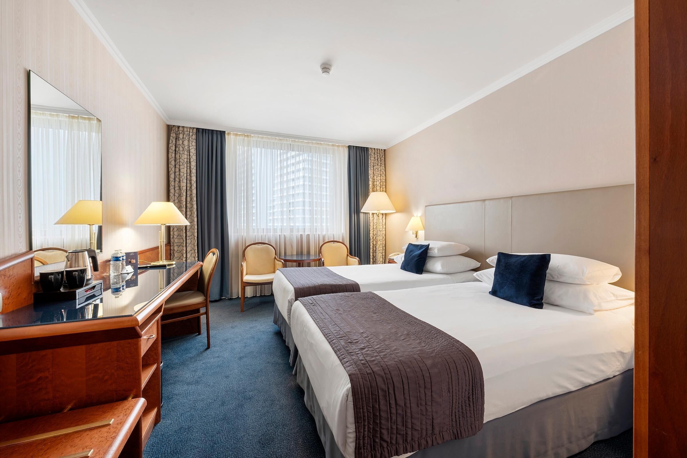 Habitación de hotel con dos camas, un escritorio, sillas, un espejo y lámparas.