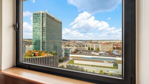 A high-rise building with a modern glass facade, viewed from a window with a wooden frame. - Panorama by Verdi Hotels (Prague)