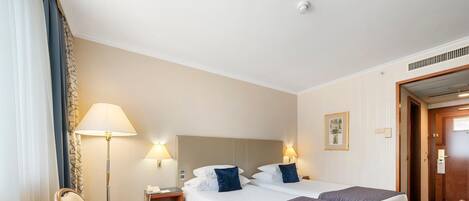 A hotel room with two beds, a desk, a chair, a lamp, and a door.