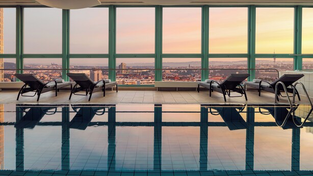 An indoor swimming pool with four lounge chairs and large windows offering a city view. - Panorama by Verdi Hotels (Prague)
