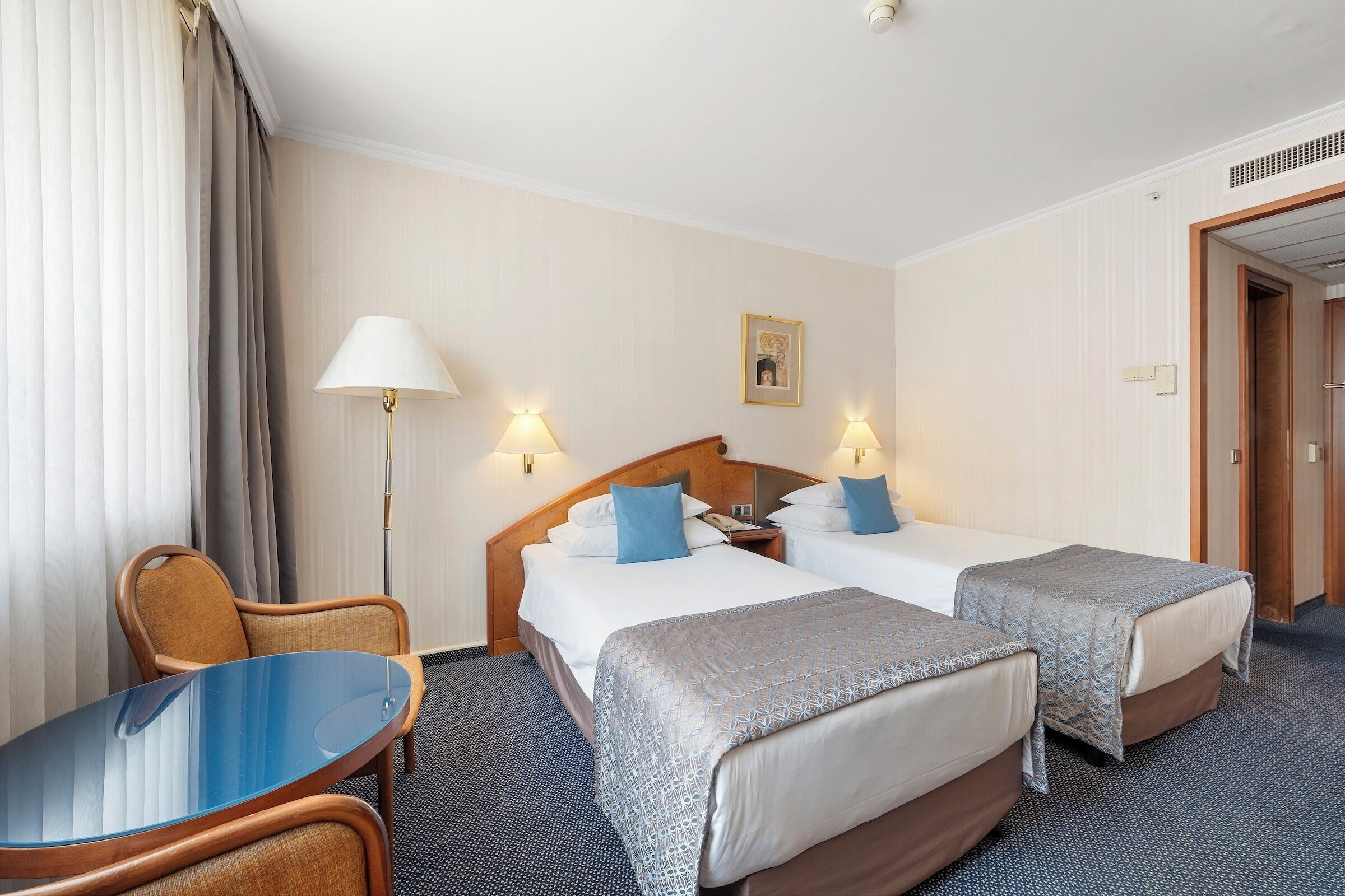 Une chambre d’hôtel avec deux lits, un bureau, une chaise et une lampe.