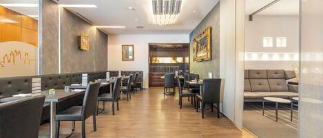 A modern restaurant with a long counter, booths, and a seating area with a sofa.