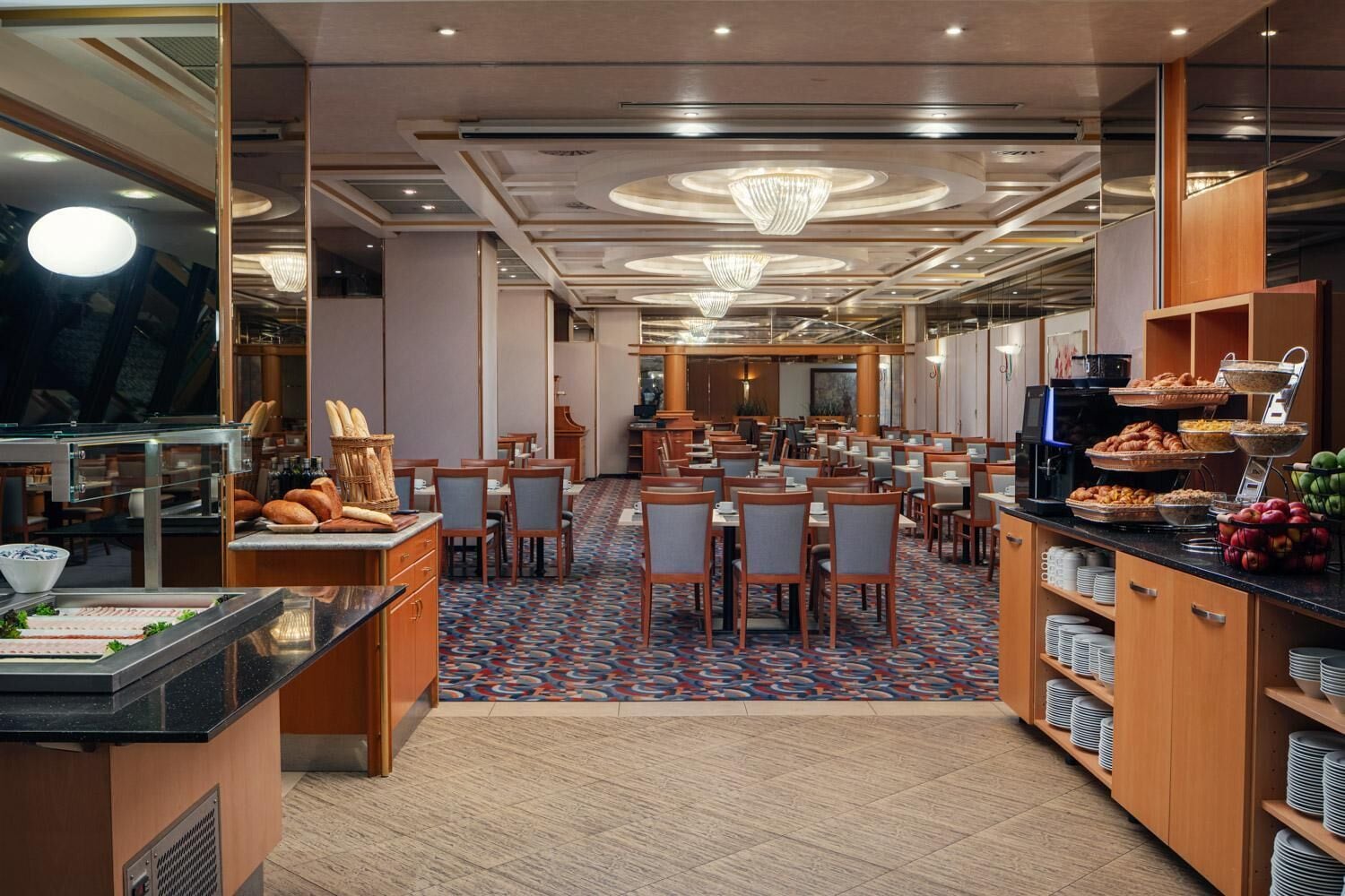Comedor de hotel con varias mesas, un bufé y distintos alimentos, además de una alfombra estampada.