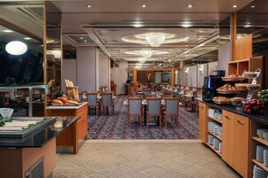 Uma sala de jantar de hotel com várias mesas, um buffet com diversos pratos e um tapete estampado.