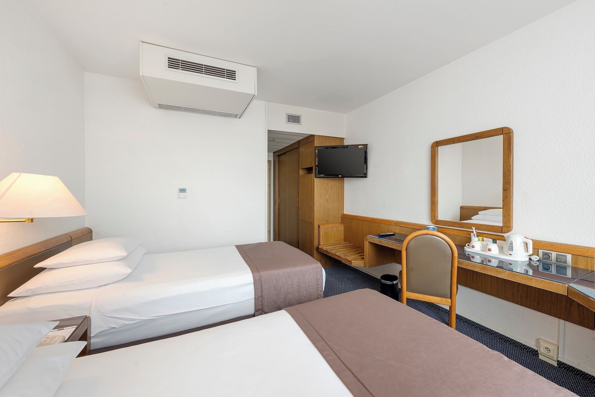 A hotel room with two beds, a desk, a chair, a television, and a mirror.
