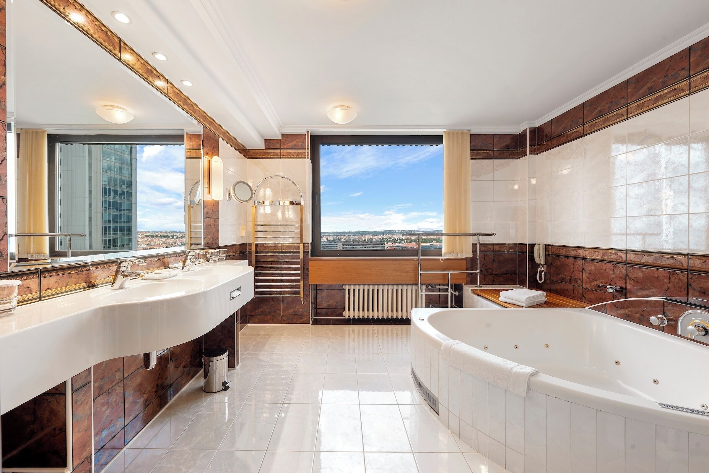 A modern bathroom with dual sinks, a large bathtub, and a view of a cityscape.