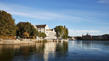 A riverside hotel with a white facade, a bridge in the background, and a calm water body.