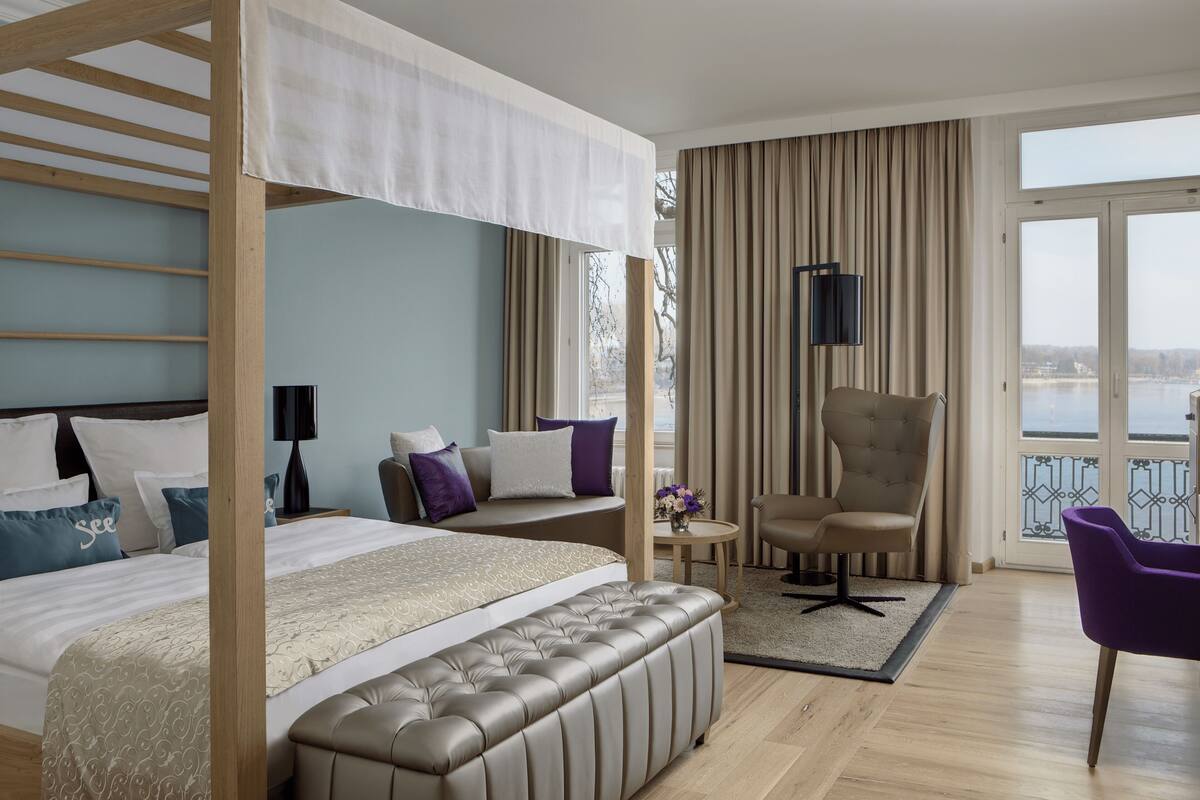 Une chambre d’hôtel avec un grand lit, un canapé, un fauteuil, une petite table et un balcon avec vue.