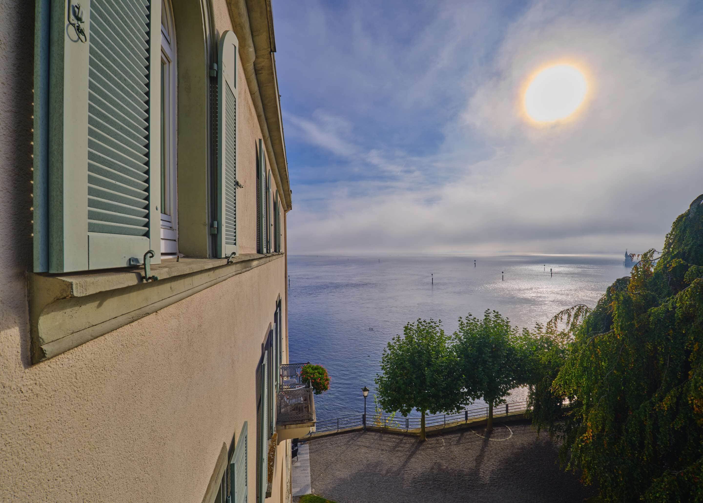 Um edifício costeiro com varanda com vista para o mar, céu claro e um navio ao longe.