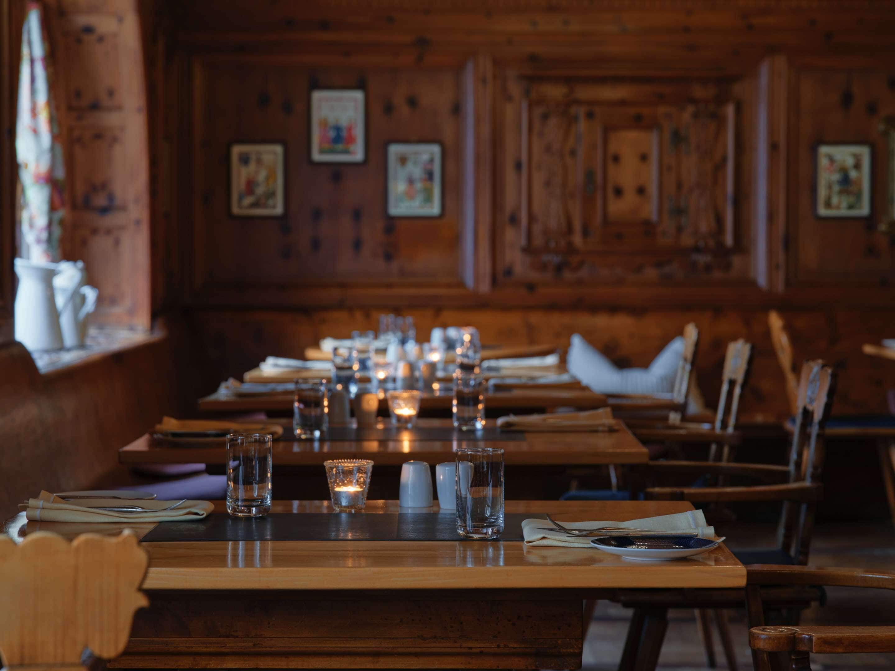 A restaurant with wooden interiors, long tables set with glasses, candles, and cutlery.