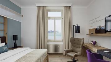 Una habitación de hotel con cama, escritorio, silla, radiador y ventana con cortinas.