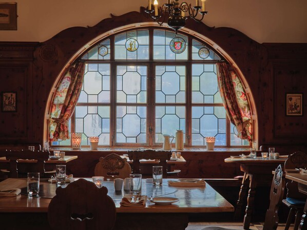 A dining area with a large arched window, wooden furniture, and a chandelier. - Steigenberger Inselhotel (Konstanz)