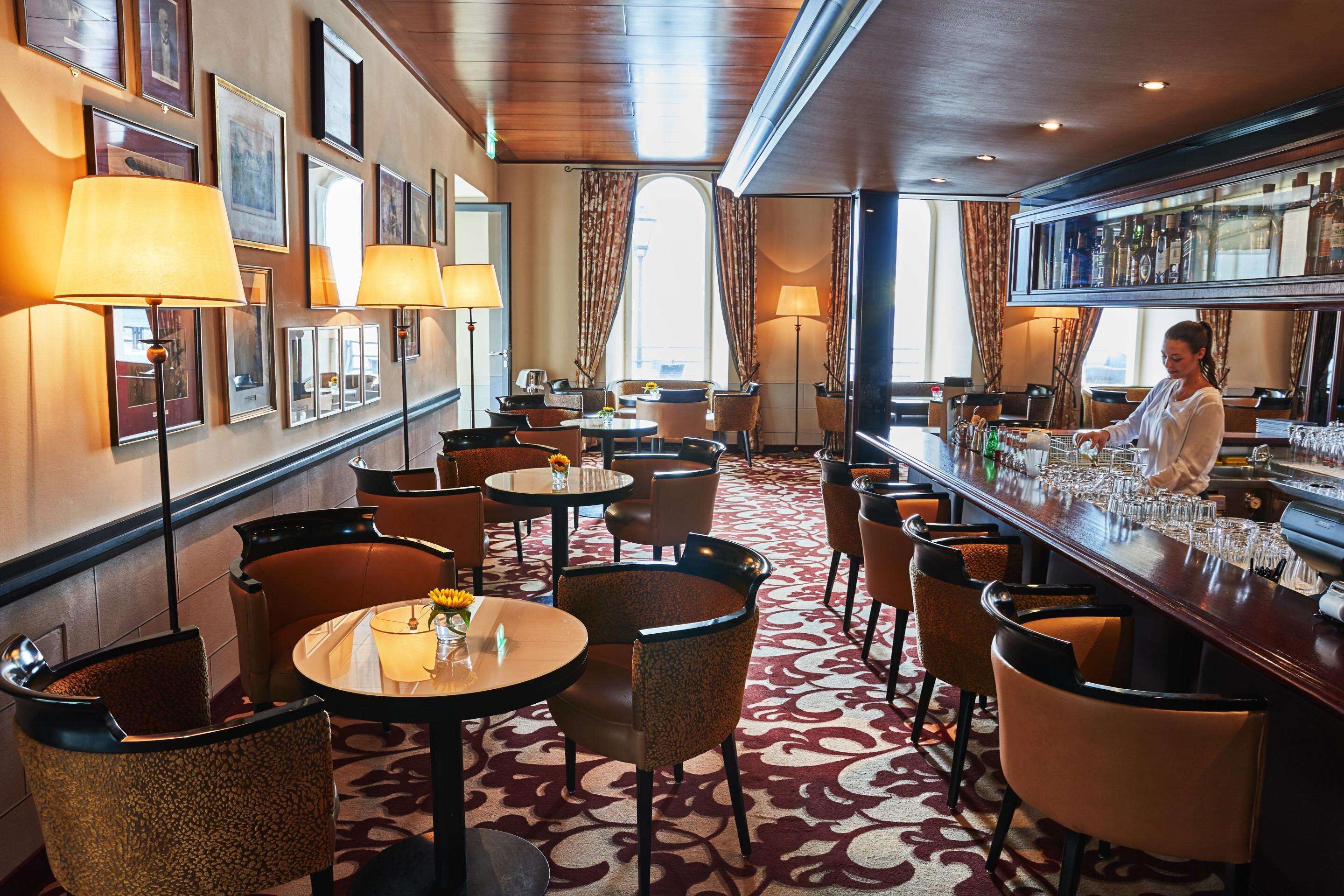 A bar area with multiple seating options, including round tables and chairs, and a bartender preparing drinks.