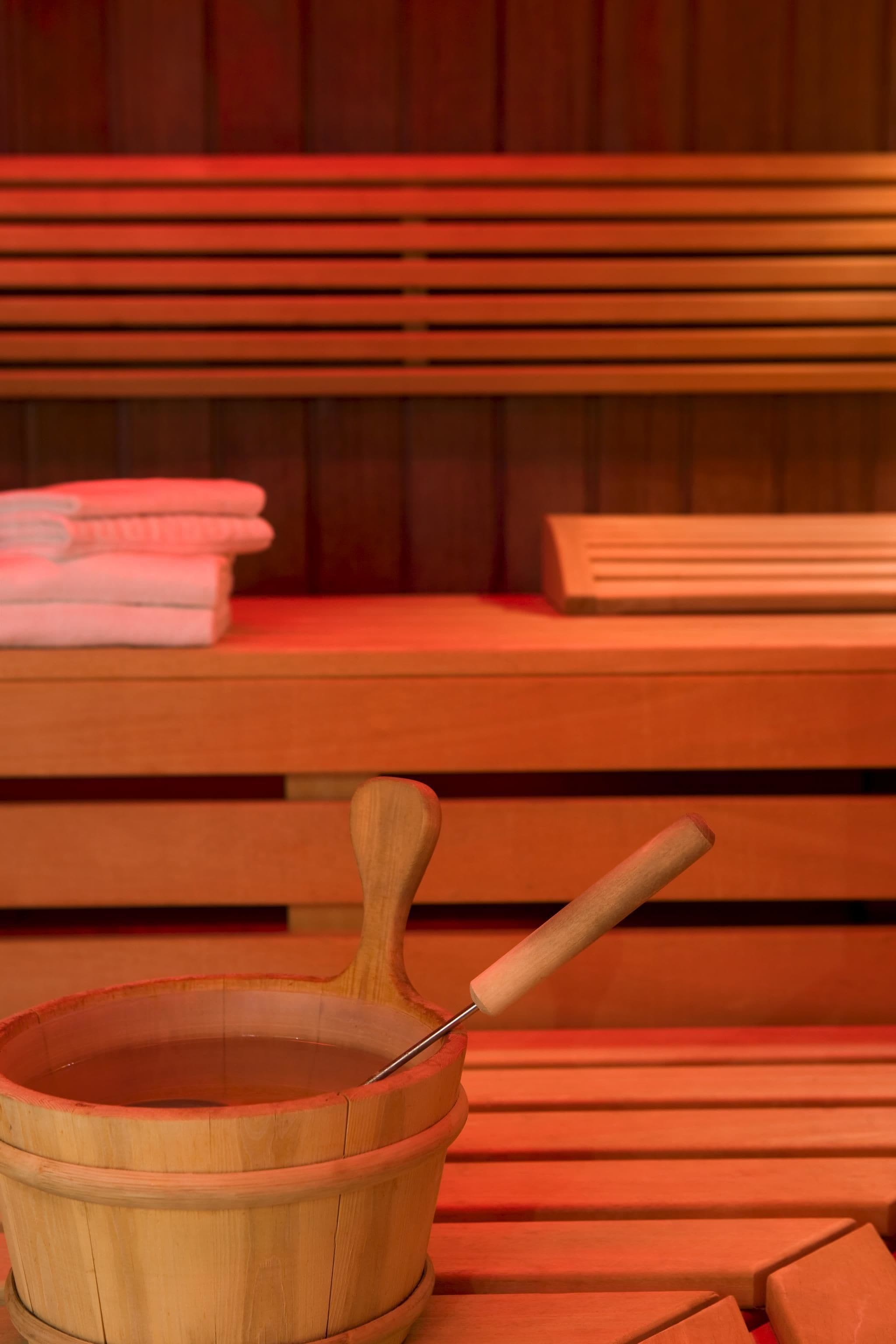 A wooden sauna bench with a wooden bucket containing a metal scoop.