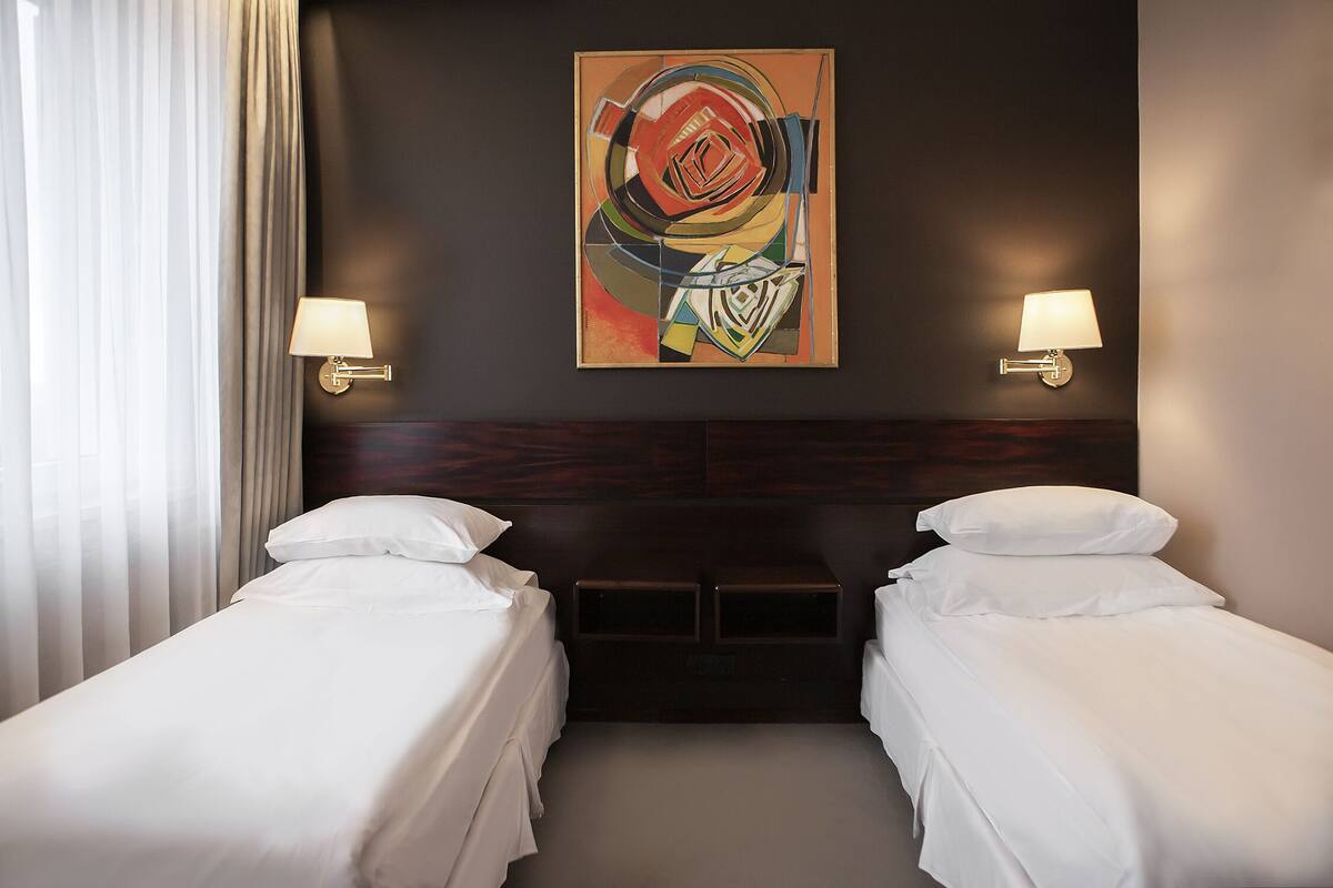Een hotelkamer met twee bedden, een groot abstract schilderij aan de muur en twee wandlampen.