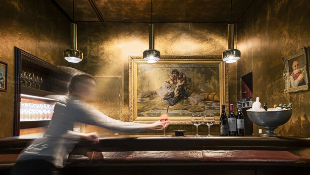 A bar area with a bartender, a painting, and a wine display.
