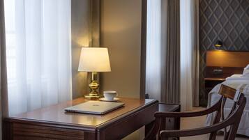 Quarto de hotel com escrivaninha de madeira, laptop, xícara e abajur.