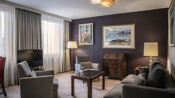 Habitación de hotel con televisión de pantalla plana, dos sillones, un sofá, una mesa de centro, un aparador y dos cuadros en la pared.