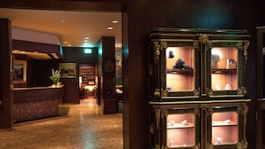 A lobby with a reception desk, a large ornate cabinet with glass doors, and a marble floor.
