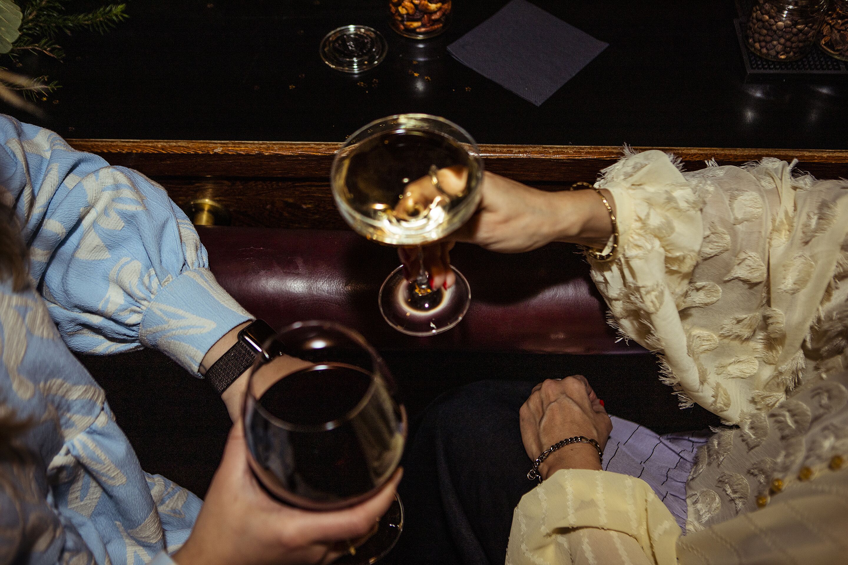 A close-up of two people holding wine glasses, seated on a leather couch.