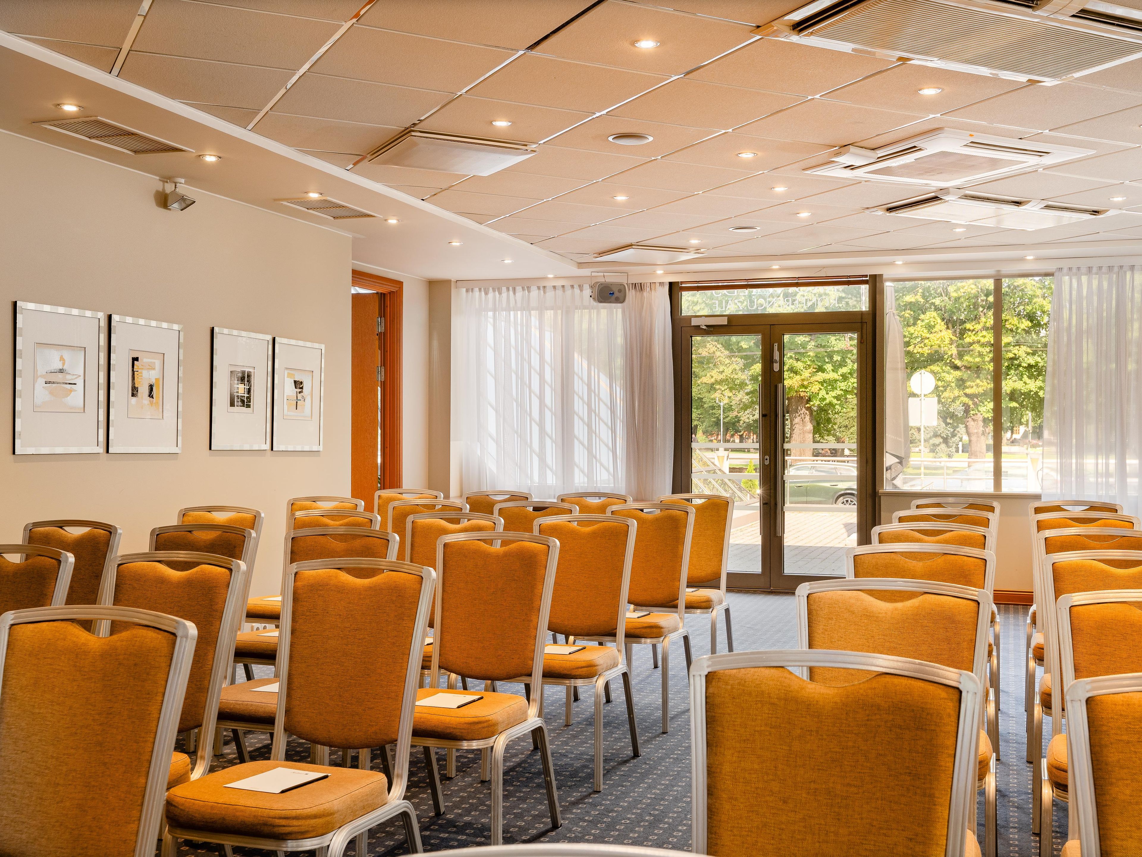 A conference room with rows of chairs, ceiling lights, and framed artwork on the wall.