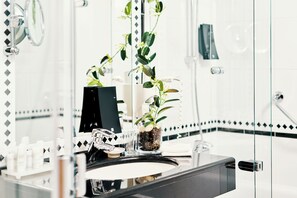 A bathroom with a large mirror, a sink, a potted plant, and a shower area.