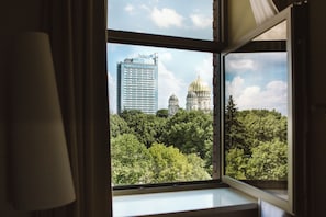 A view from a window overlooking a cityscape with a prominent building and a domed structure amidst dense greenery.