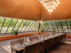 A restaurant with a long dining table, chairs, and a chandelier.