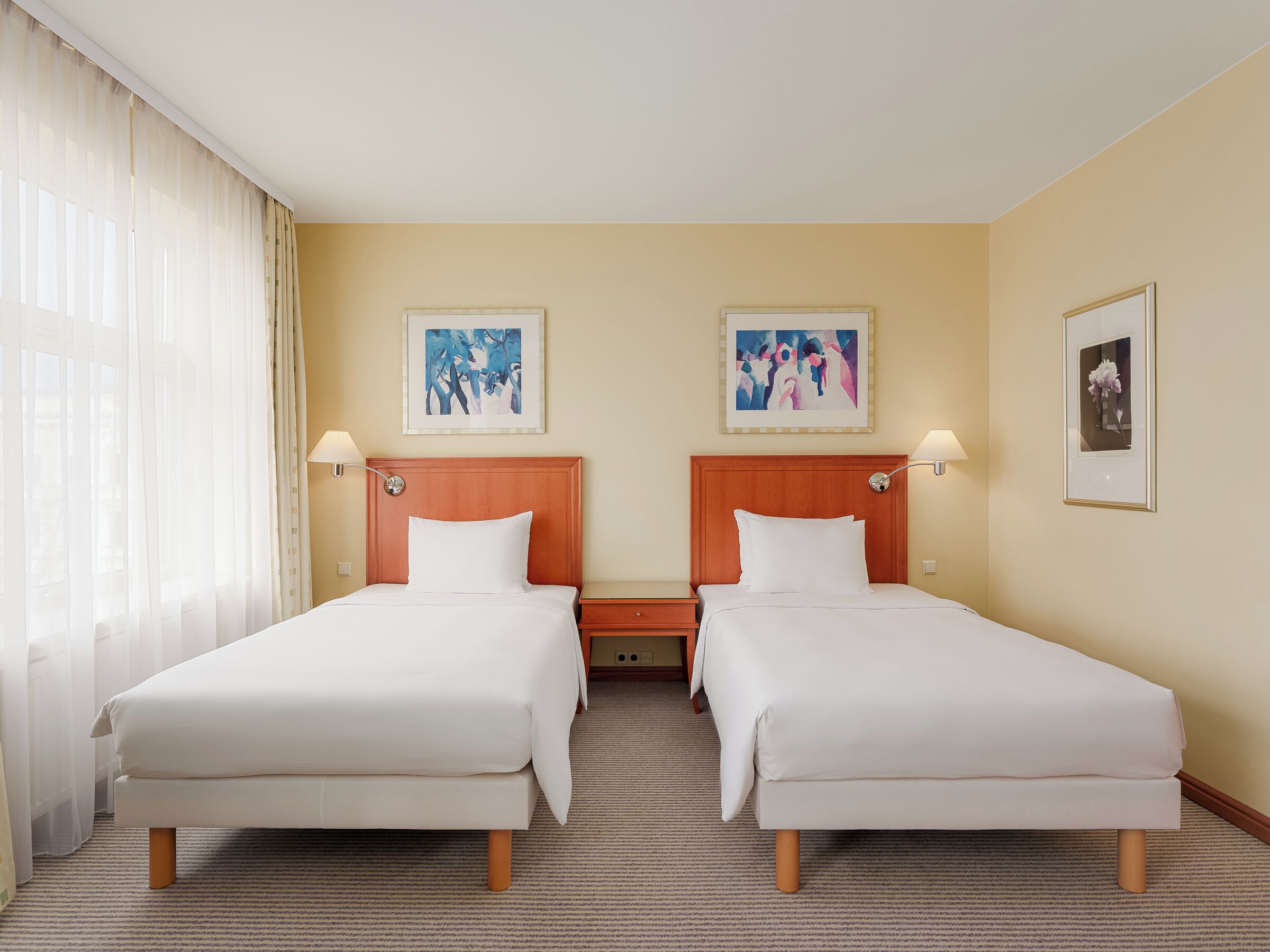 Ein Hotelzimmer mit zwei Einzelbetten, einem Holzkopfteil, Teppichboden und zwei gerahmten Bildern an der Wand.