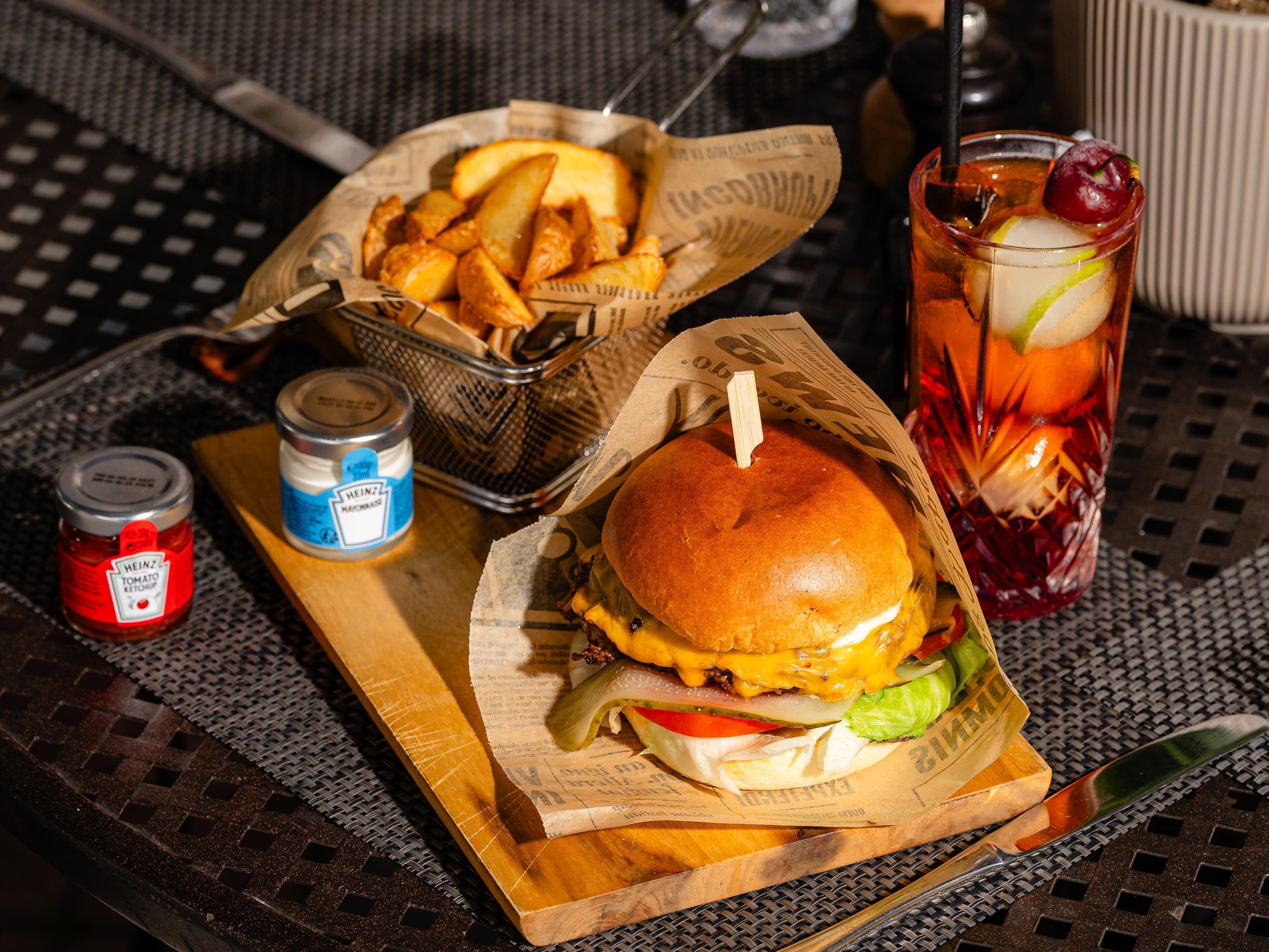 Een maaltijd bestaande uit een hamburger, friet en een drankje, geserveerd op een tafel met een krant en bijgerechten.