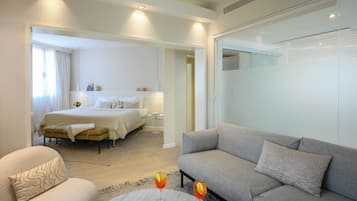 Une chambre d’hôtel avec un lit, un canapé, une petite table avec une boisson et un livre, et une vue sur le couloir.