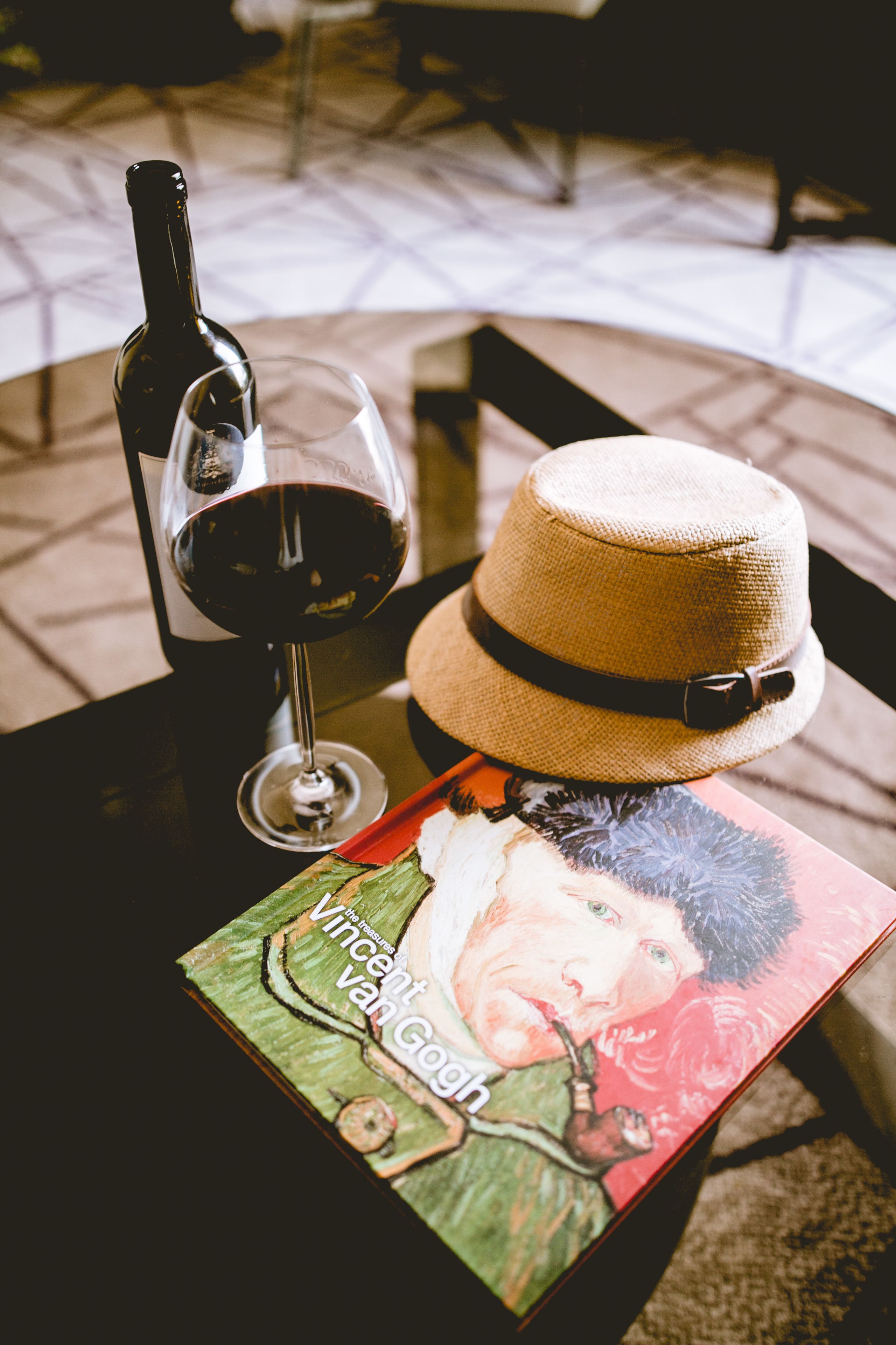 Eine Flasche Rotwein, ein Glas und ein Hut auf einem Tisch mit einem Buch mit dem Titel "Vincent van Gogh".
