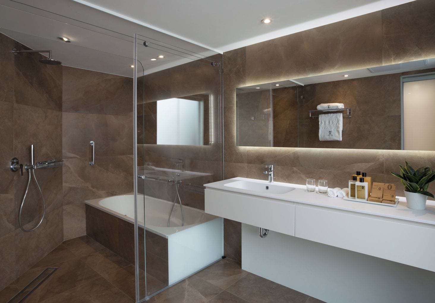 A modern bathroom with a glass-enclosed shower, a large mirror, and a vanity with toiletries.