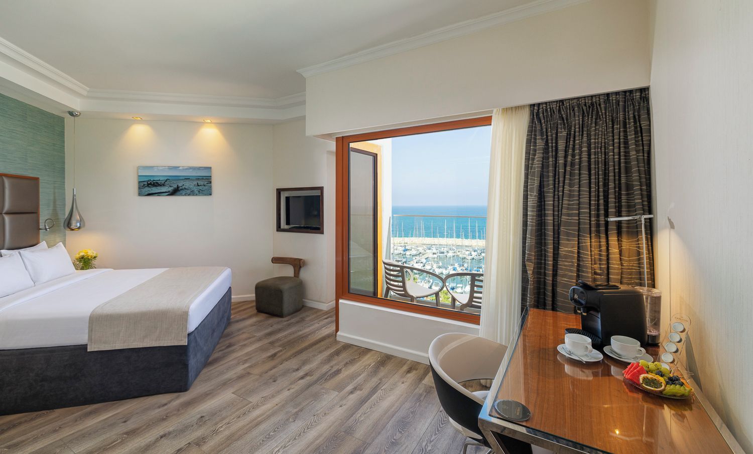 Ein Hotelzimmer mit Bett, Schreibtisch mit Kaffeemaschine, Meerblick und kleinem Fenster mit Vorhängen.