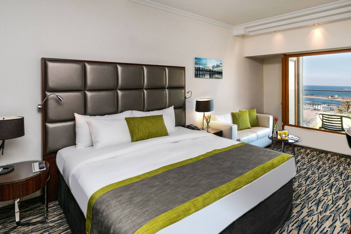 A hotel room with a large bed, a desk, a chair, and a view of the beach.