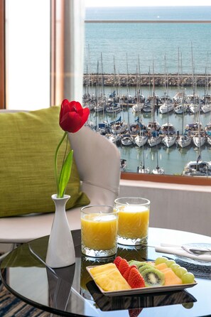 A breakfast table with fruit, juice, and a vase with a flower, overlooking a marina with boats. - Carlton Tel Aviv Hotel (Tel Aviv)