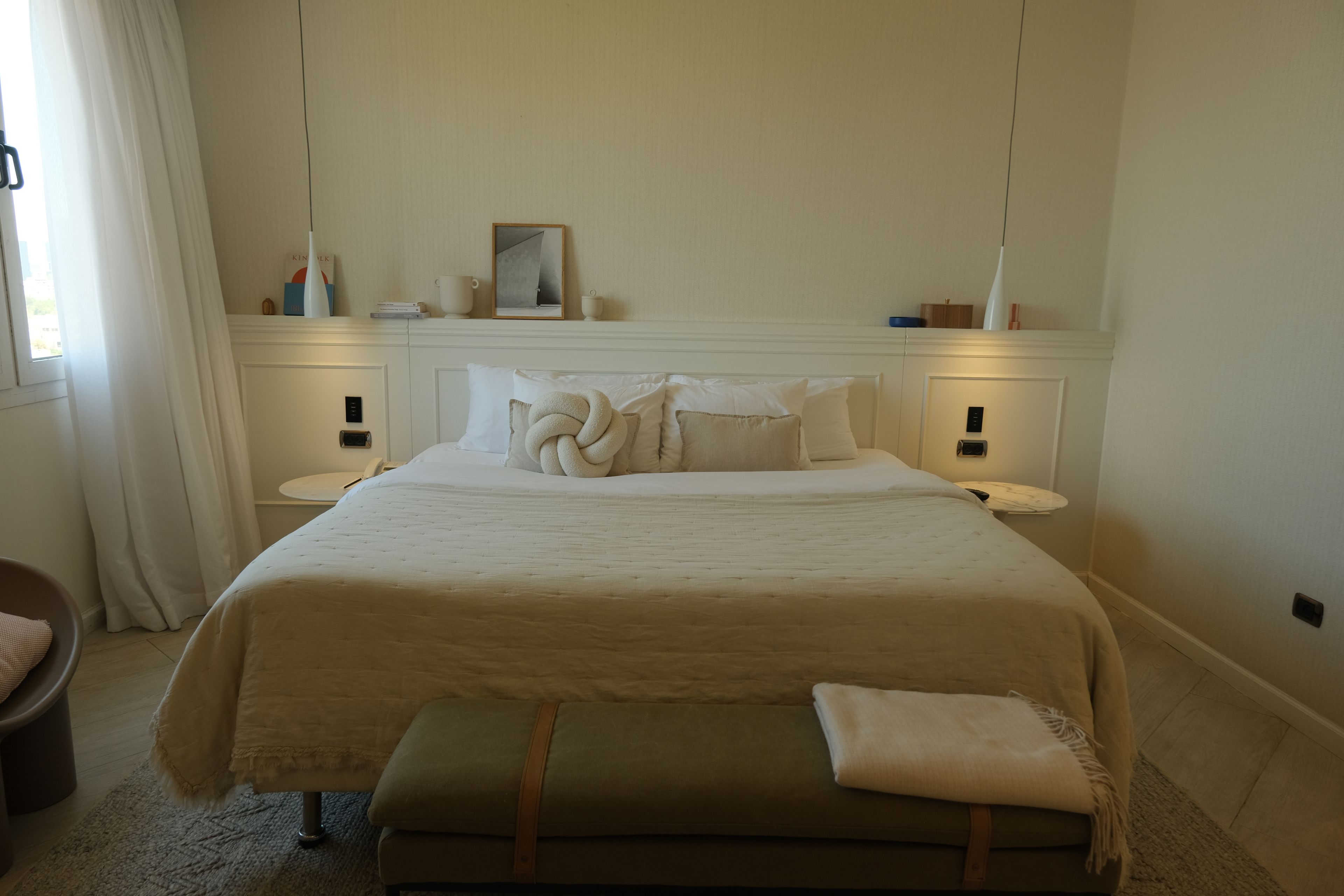 Een keurig opgemaakte slaapkamer met een groot bed, nachtkastjes, een bedlampje en een raam met gordijnen.