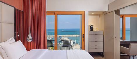 A hotel room with a bed, a desk, a chair, and a view of the sea.