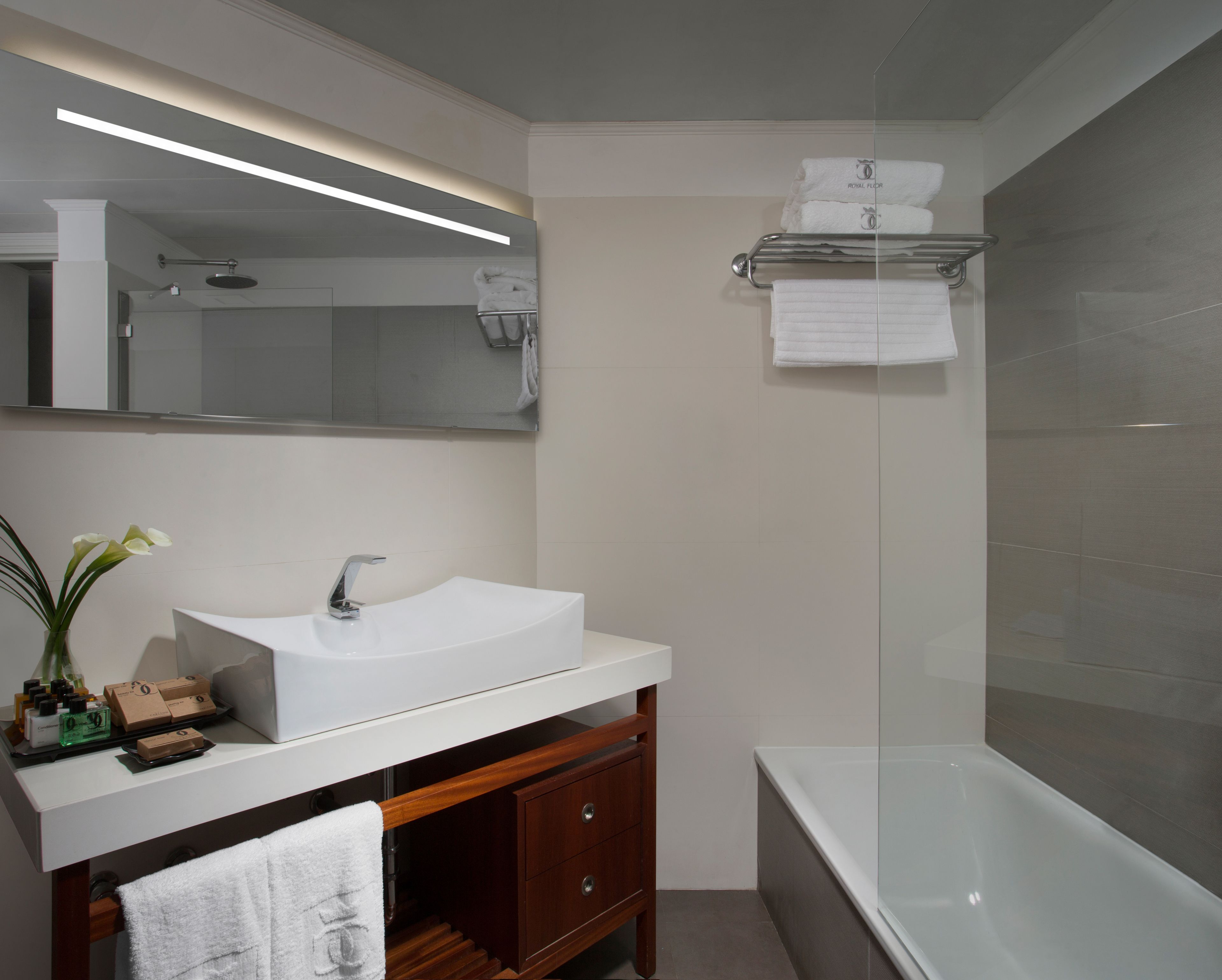 Un baño moderno con un lavamanos, tocador blanco y una bañera con mampara de vidrio.