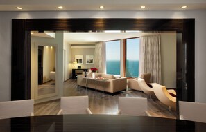 Una habitación de hotel moderna con zona de comedor, un conjunto de sofás, una mesa de centro y vista al océano.