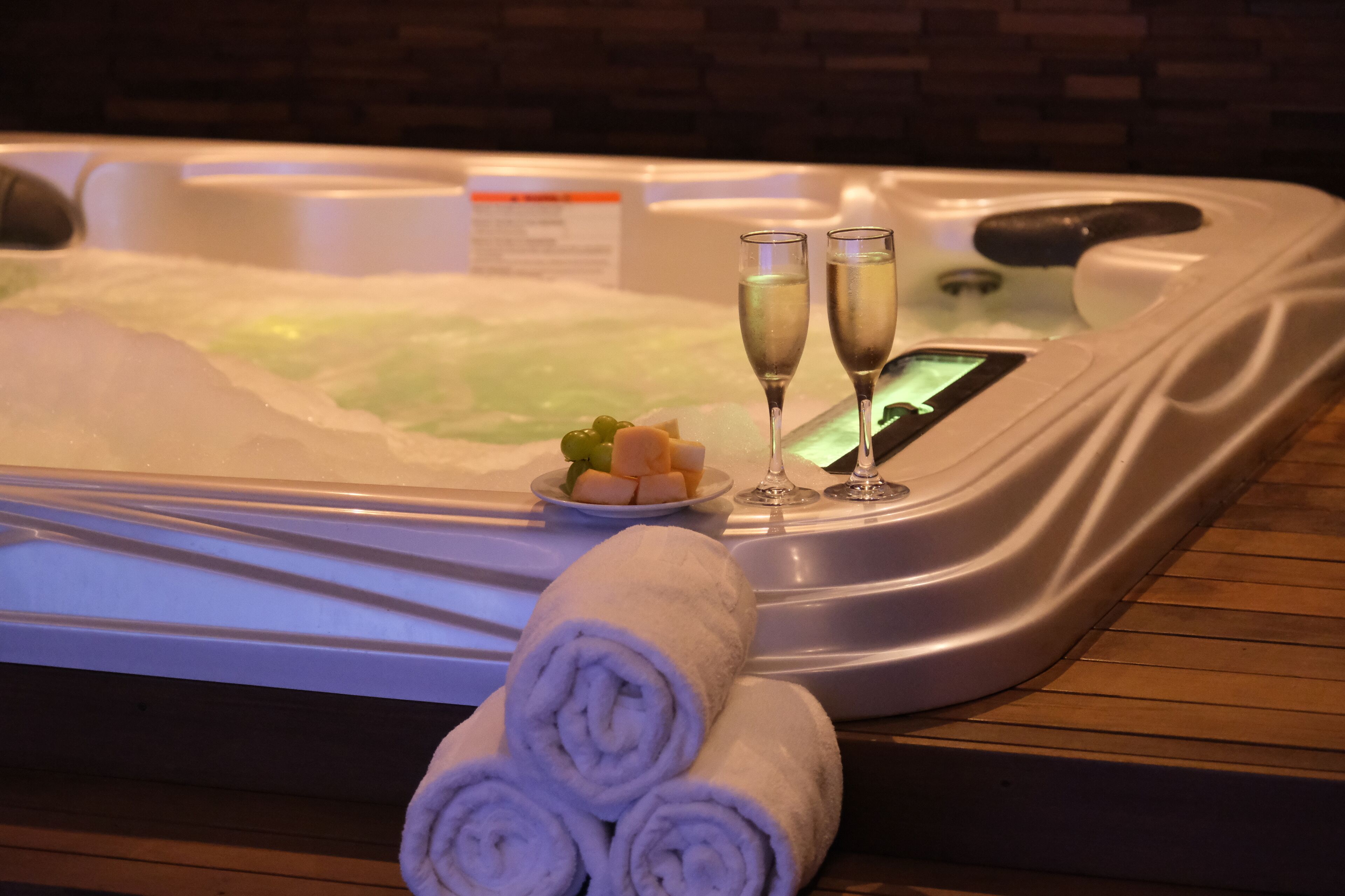 A hot tub with two glasses of champagne, a plate of fruit, and rolled towels.