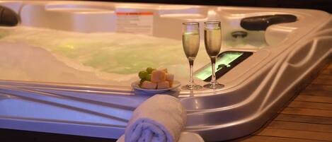 A hot tub with two glasses of champagne, a plate of fruit, and rolled towels.