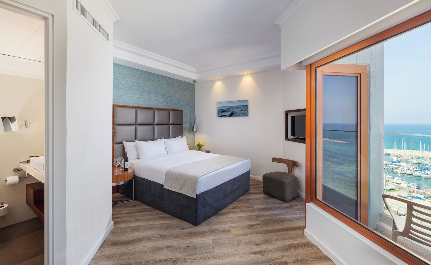 A hotel room with a bed, bedside table, and a view of the sea through a large window.